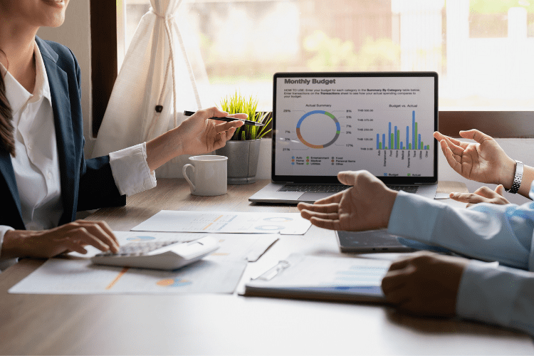 A group of chartered accountants conducting an audit around a table with a laptop and graphs on it.